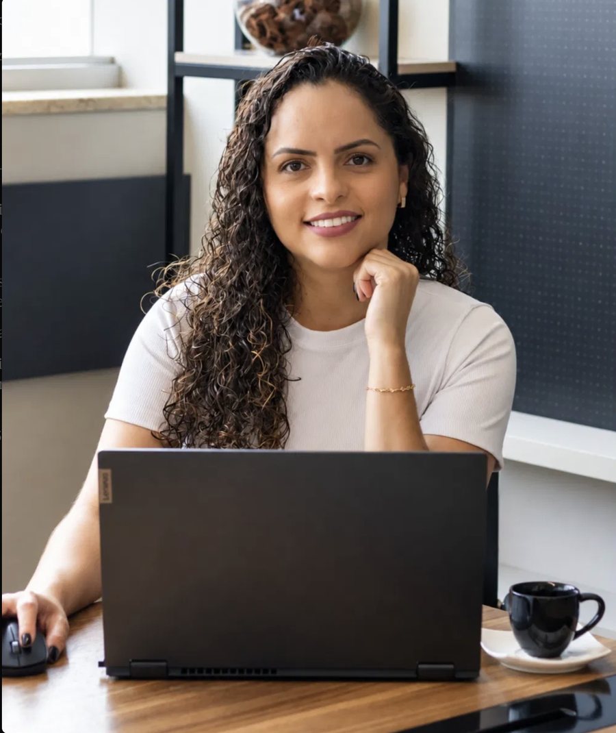 Foto da psicóloga Nayara Ferreira sorrindo, sentada à mesa com um notebook